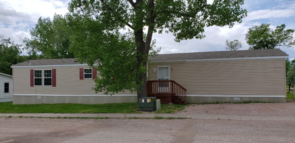 mobile home with beige siding and a tree next to a red starcase